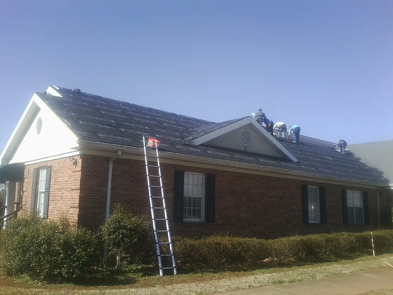 Crew tearing shingles off a brick ranch roof with a ladder set — Metal Roof Repair work by our crew in Rayle