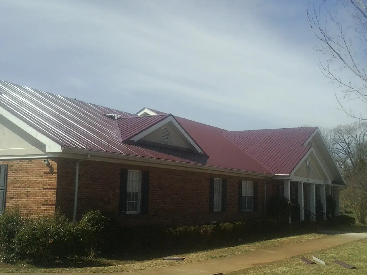 Red metal roof with gabled entries on a long brick building, from a Hail Damage Roof Repair job in Rayle