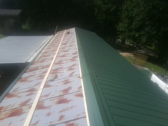 Old rusted panels beside newly installed green metal roofing in Rayle