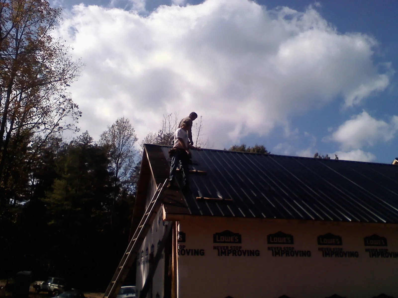 Roofer fastening dark metal panels high against a cloudy sky, from a Roof Inspection job in Rayle